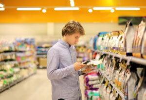 Man, shopping in supermarket reading product information. Using smart phone for Pet food