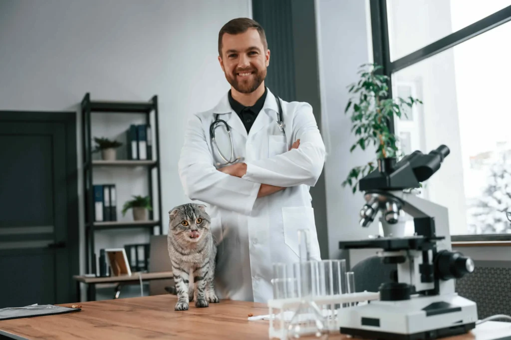 A Doctor in a white coat standing next to a gray cat on a table, surrounded by lab equipment like a microscope.
