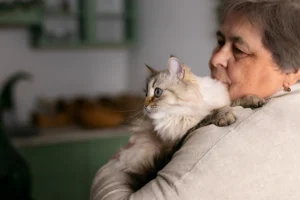 An older woman holding a fluffy white and gray cat, both looking off to the side.