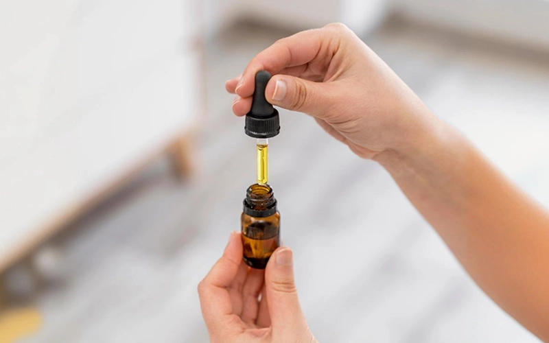 A close-up of hands holding a dropper of CBD oil