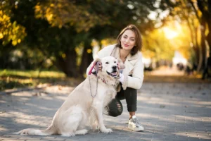 A young woman kneeling beside her Golden Retriever during a walk in the park, showcasing the strong bond between the pet and its owner.