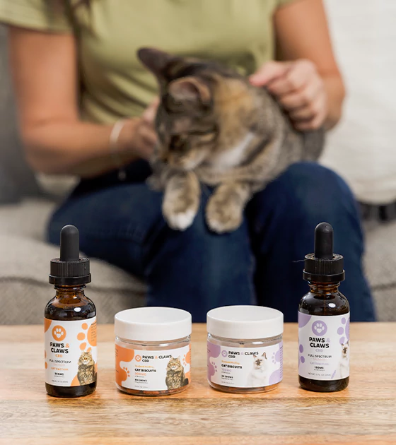A person pets a cat on a couch while four Paws & Claws pet care products